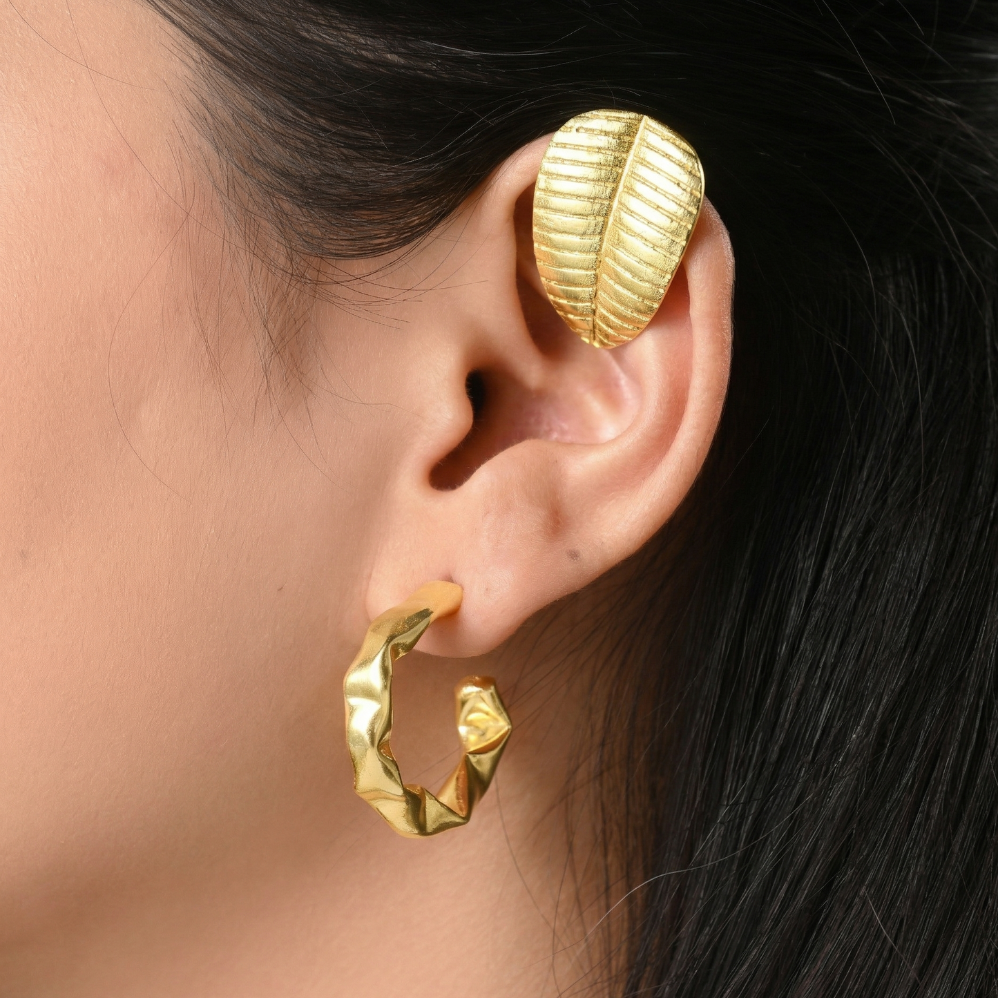 Gold hoop earrings and a gold cuff in the shape of a leaf 