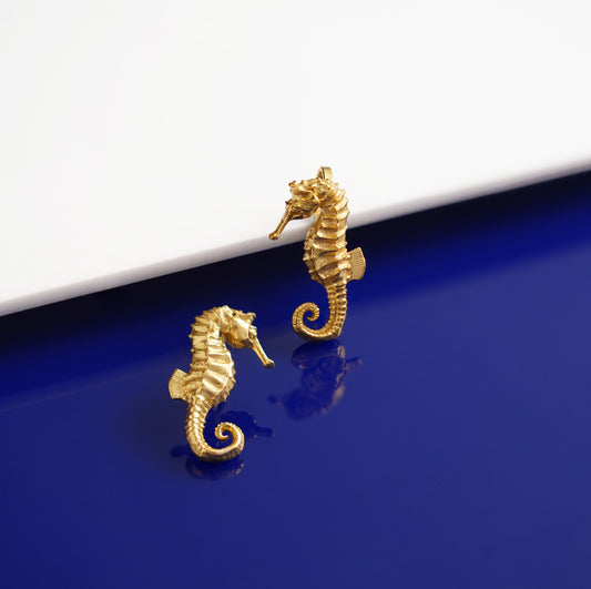 Gold seahorse earrings on a blue and white background